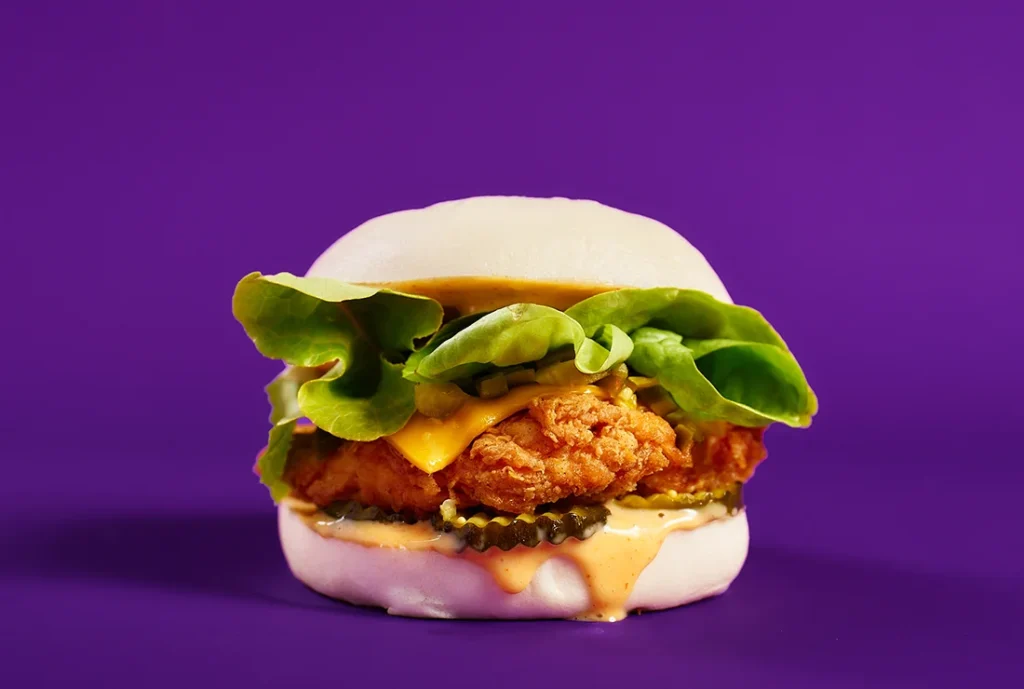 YOMG Firebird Bao Crispy Spicy Fried Chicken Burger Menu Item - spicy fried chicken, cheese, bacon, pineapple, lettuce, tomato, avocado mayo, purple bun