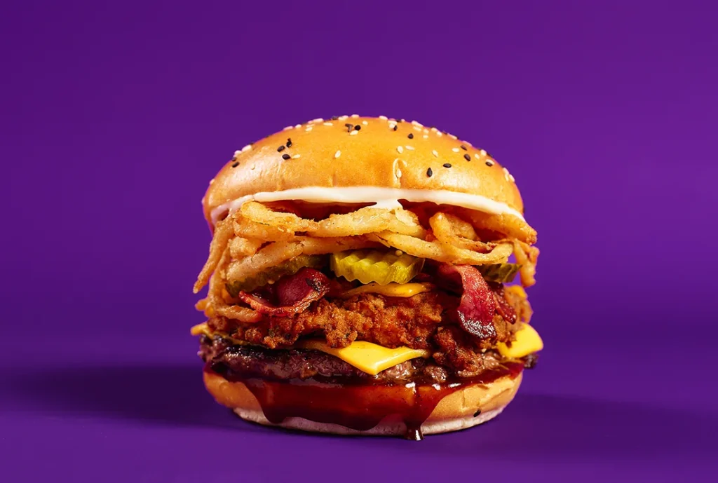 YOMG The Muffler Angus Beef Southern Fried Chicken Burger Menu Item - beef, southern fried chicken, double cheese, bacon, pickles, onion fries, BBQ sauce, mayo